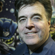 Neal Adams smiles at the camera with a mural of DC superheroes behind him.